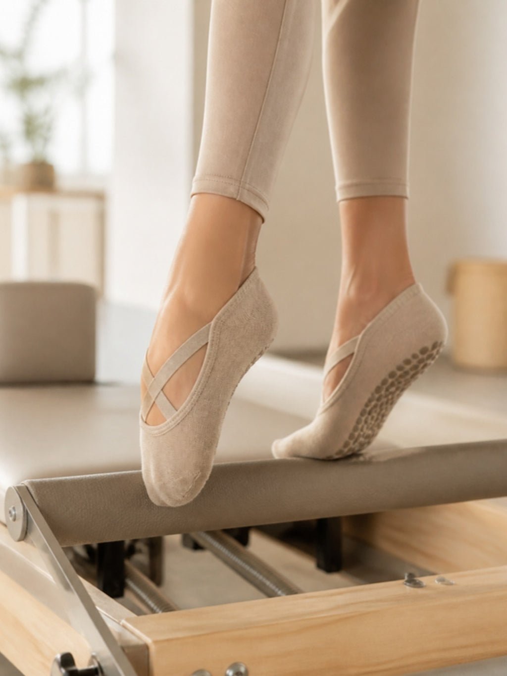 Chaussettes grip Ancrée beiges portées sur un Reformer de Pilates, bandes croisées et picots en silicone